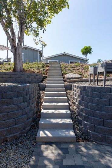 Concrete stairs leading up a landscaped hillside to a house with trees and blue sky