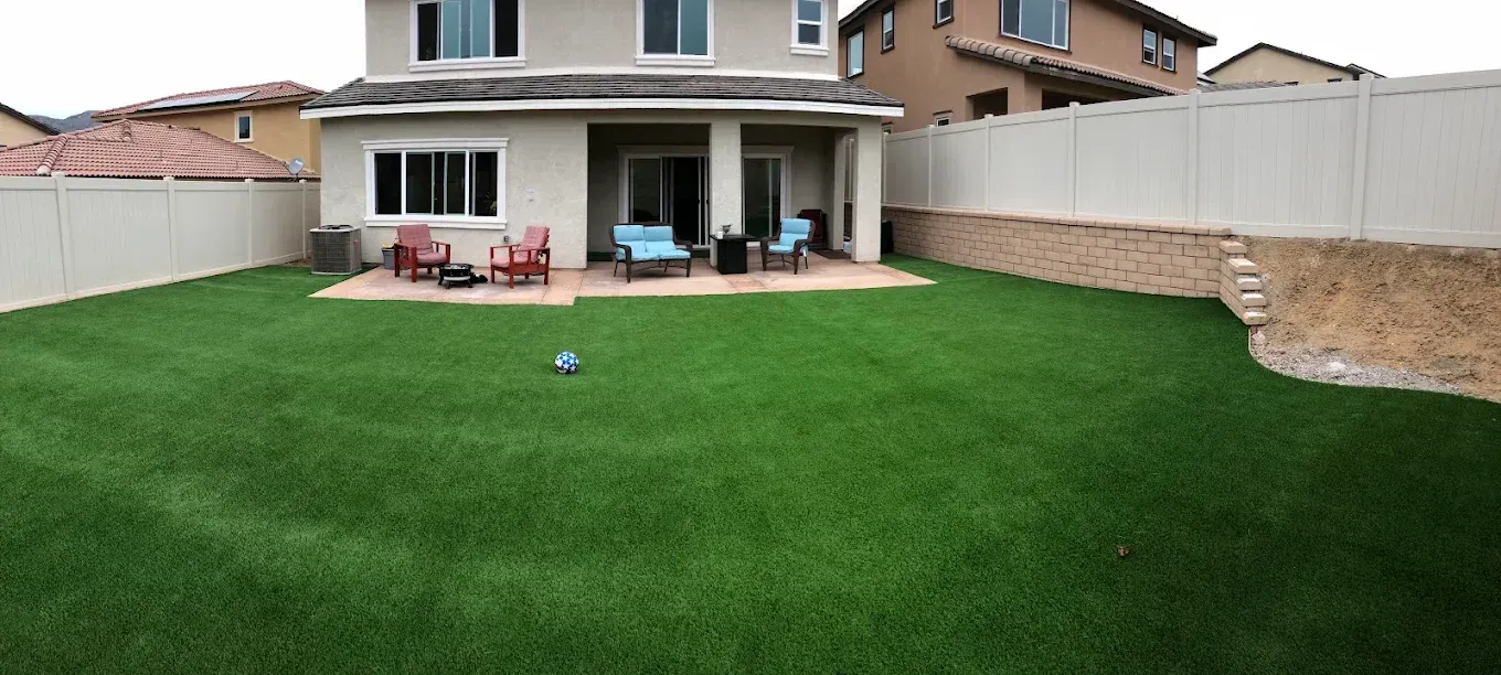 Backyard with green lawn, patio furniture, and a two-story house in the background