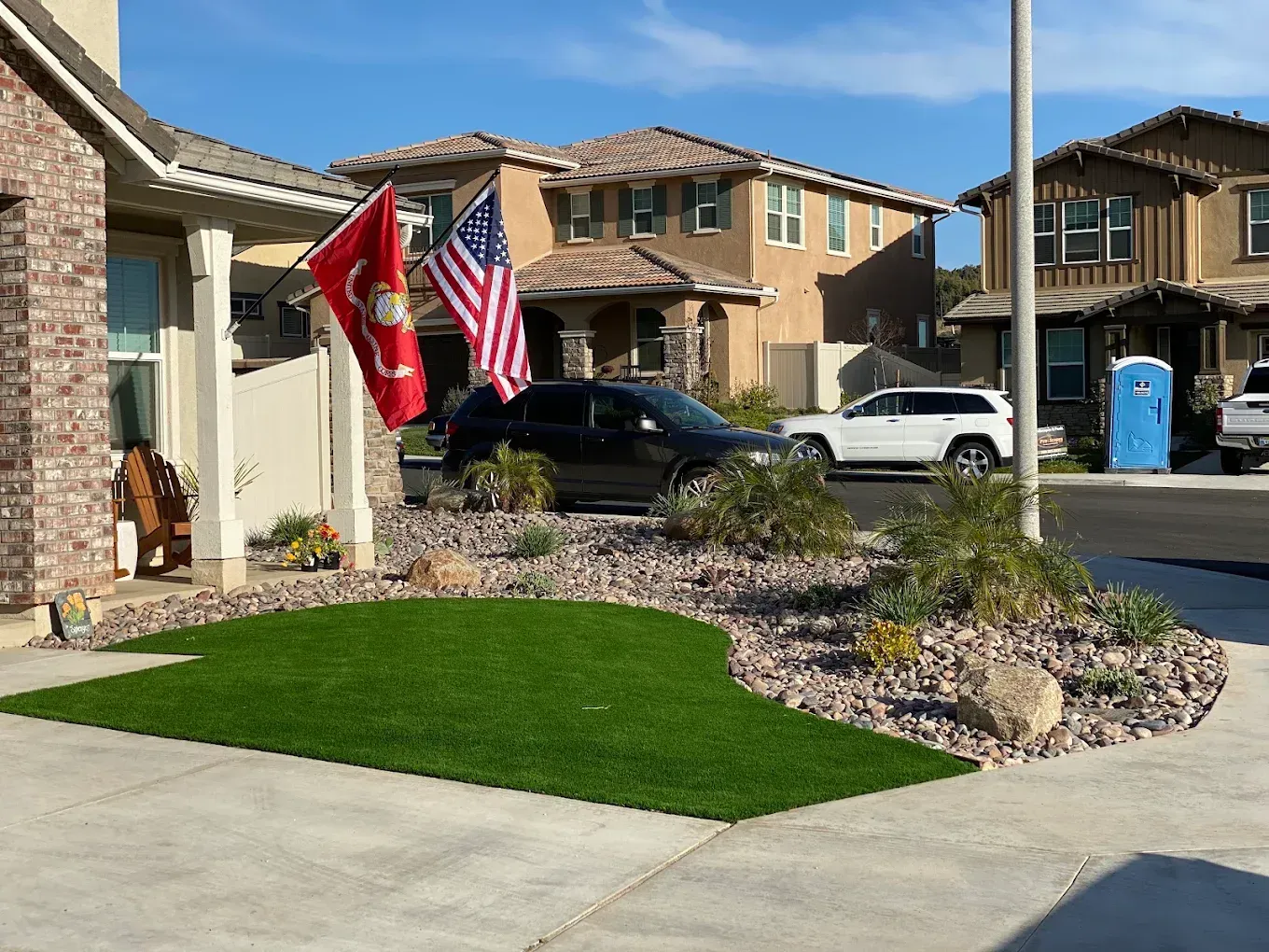 Suburban front yard with two flags, a black SUV, and a white truck outside tan houses