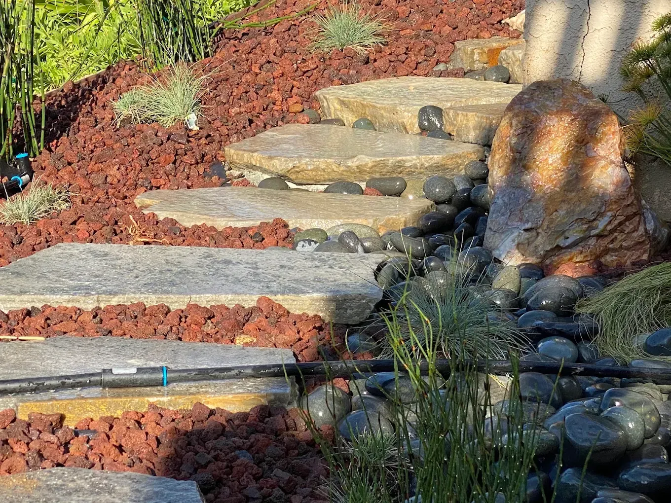 Stone steps with red mulch and rocks in a landscaped garden, dappled by tree shadows.