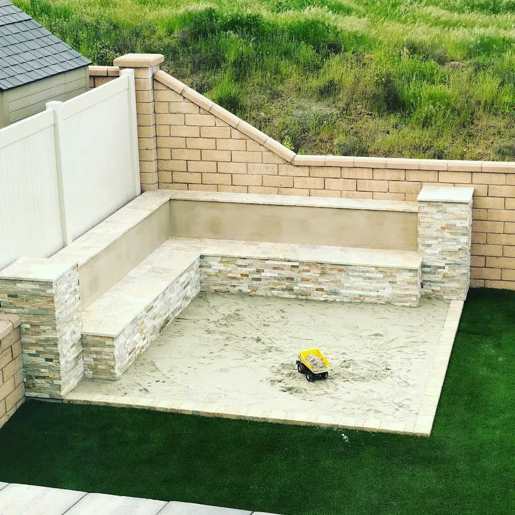 Partially built backyard patio with stone walls, concrete slab, and a yellow tool on the floor