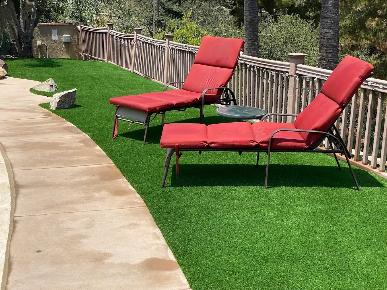 Two red lounge chairs on a green lawn beside a curved stone patio and wooden fence