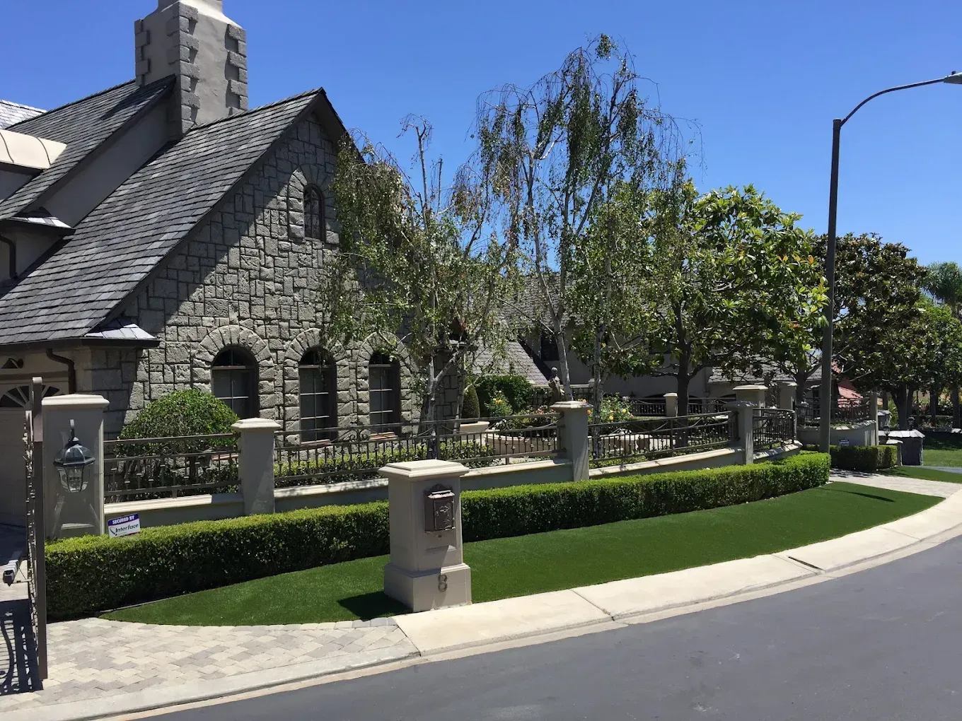 Stone church with a steep roof beside a manicured lawn and curved street under a clear blue sky