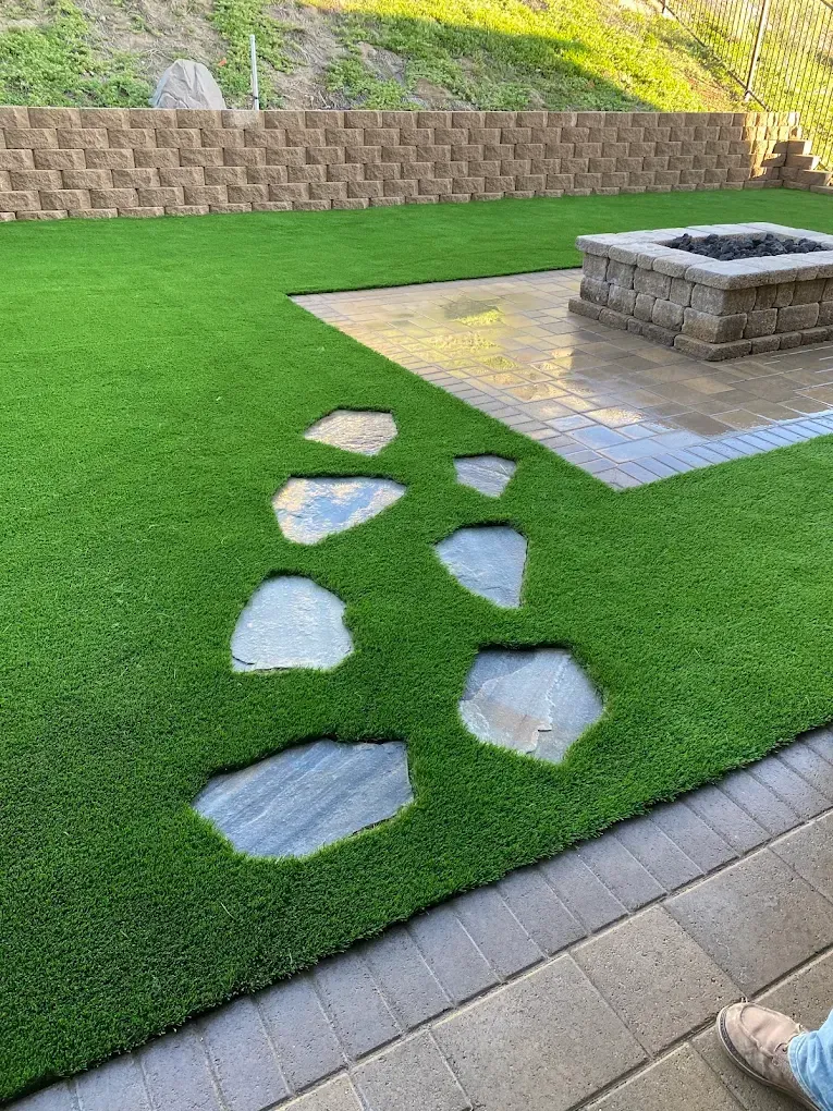 Backyard lawn with stepping stones leading to a raised stone fire pit on a concrete pad
