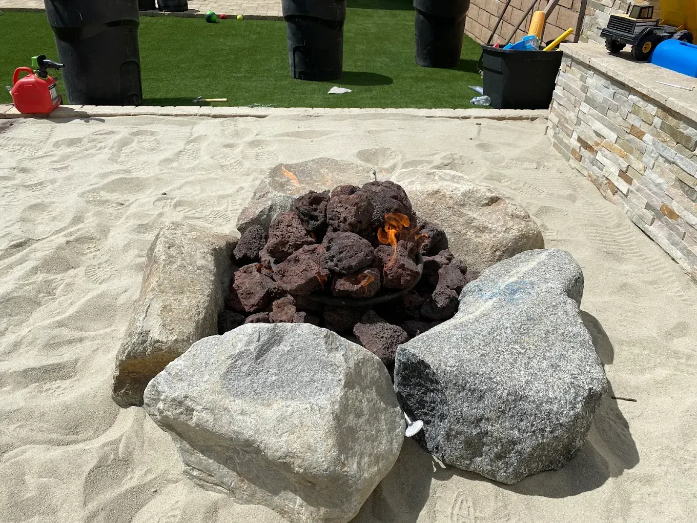 Stone fire pit with glowing coals and flames on a patio, surrounded by large rocks.