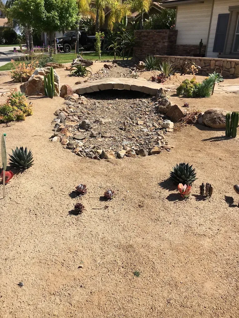Desert-style front yard with rocks, succulents, and a small stone bridge over a dry creek bed