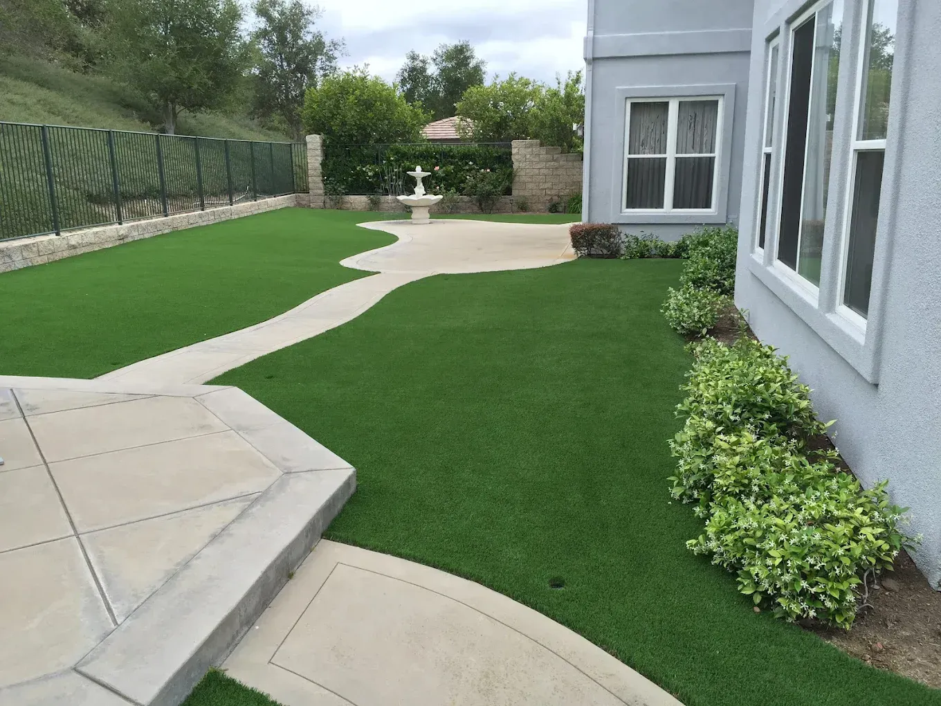 Landscaped backyard with artificial turf, curving stone path, and patio beside a house