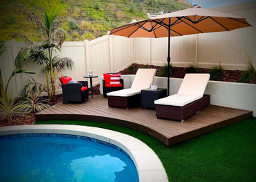 Backyard pool patio with lounge chairs, umbrella, and wicker seating beside a curved pool