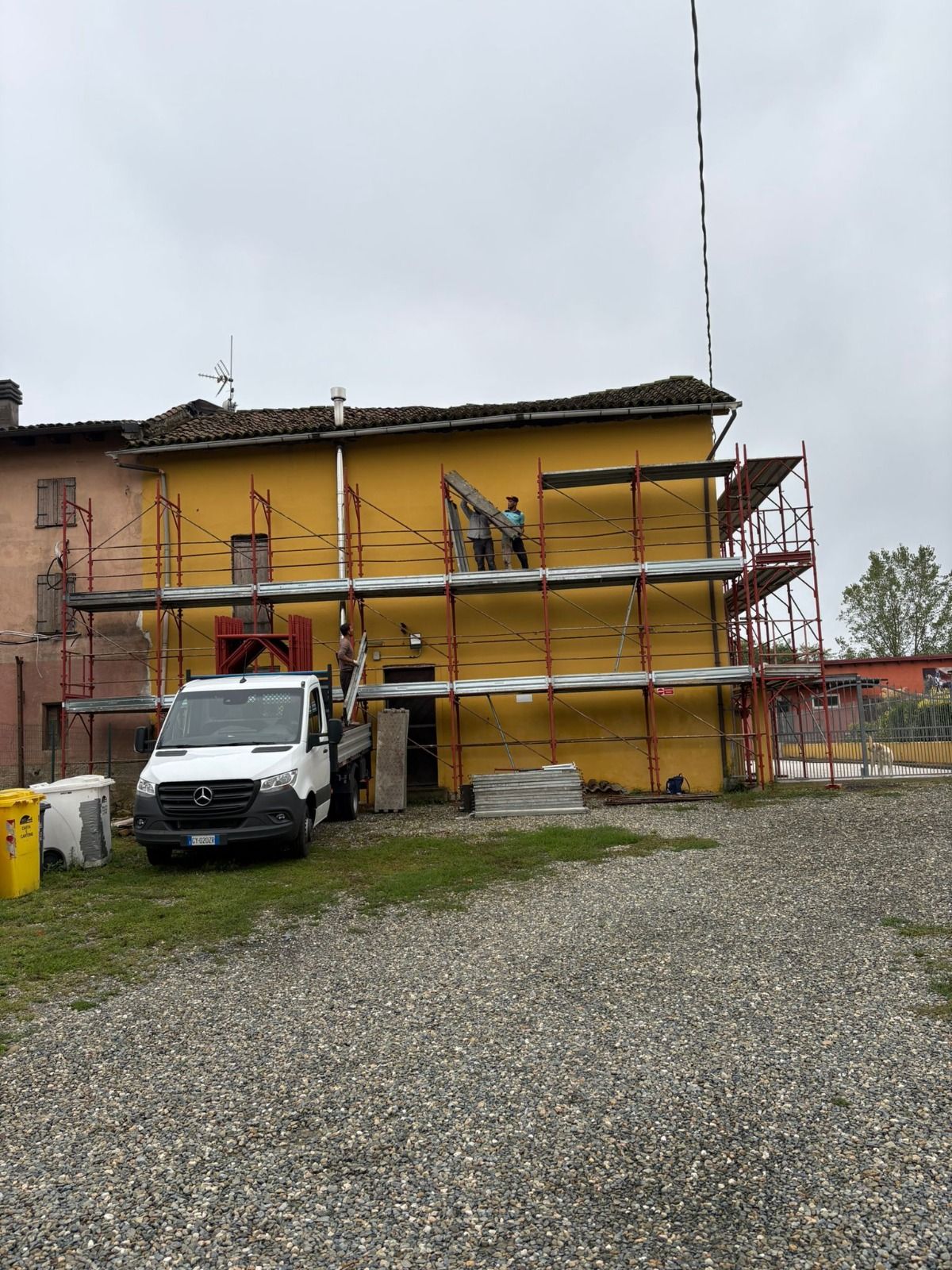 Edificio giallo in fase di ristrutturazione con impalcature e un camion bianco parcheggiato di fronte.