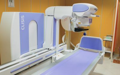 Sala di diagnostica per immagini con lettino per pazienti viola e scanner TC bianco su pareti arancioni.