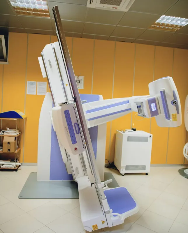 Apparecchio radiografico medicale in una stanza clinica con pareti arancioni e piattaforma per il paziente.