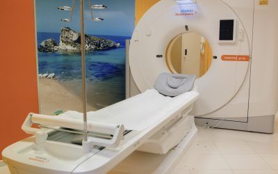 Sala per risonanza magnetica con lettino per il paziente e parete in vetro con murale raffigurante una spiaggia tropicale.