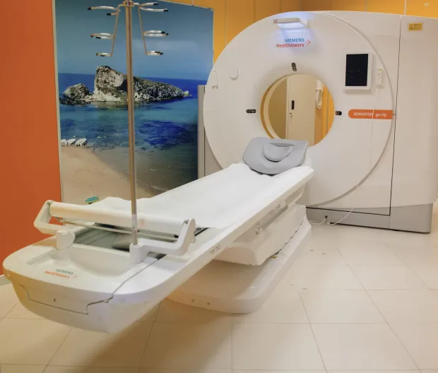 Sala per la TAC con apparecchiatura di diagnostica per immagini bianca e lettino per le visite, accanto a un murale raffigurante una spiaggia.