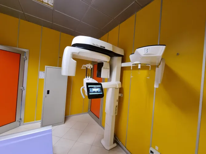 Una macchina per la risonanza magnetica in una stanza medica di colore giallo brillante, con schermo per il paziente e unità di controllo.
