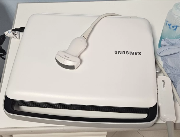 Un computer portatile Samsung bianco con un cavo di ricarica bianco sopra, appoggiato su una scrivania vicino a una bottiglia d'acqua.