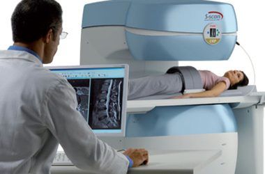 Un tecnico di risonanza magnetica osserva le scansioni mentre un paziente è sdraiato sul lettino dello scanner.