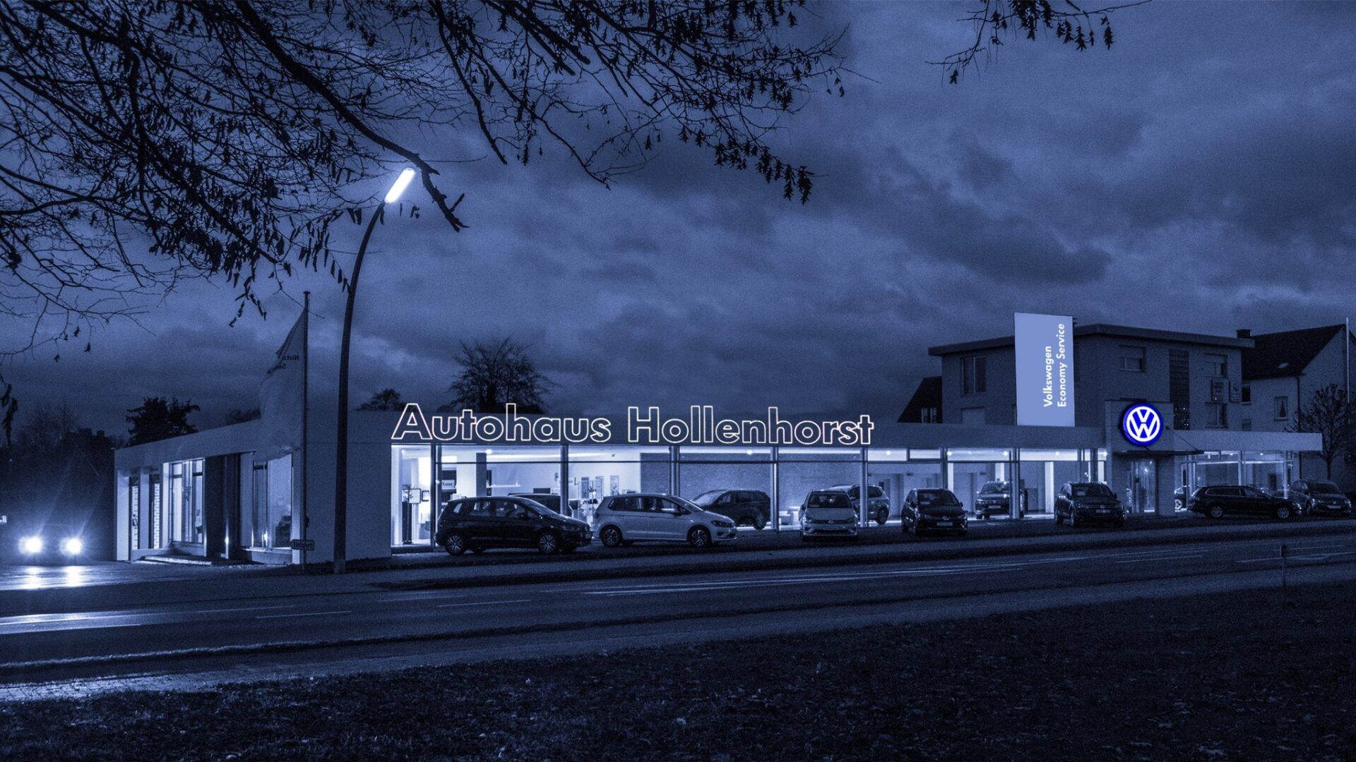 Ein Autohaus ist nachts beleuchtet und davor parken Autos