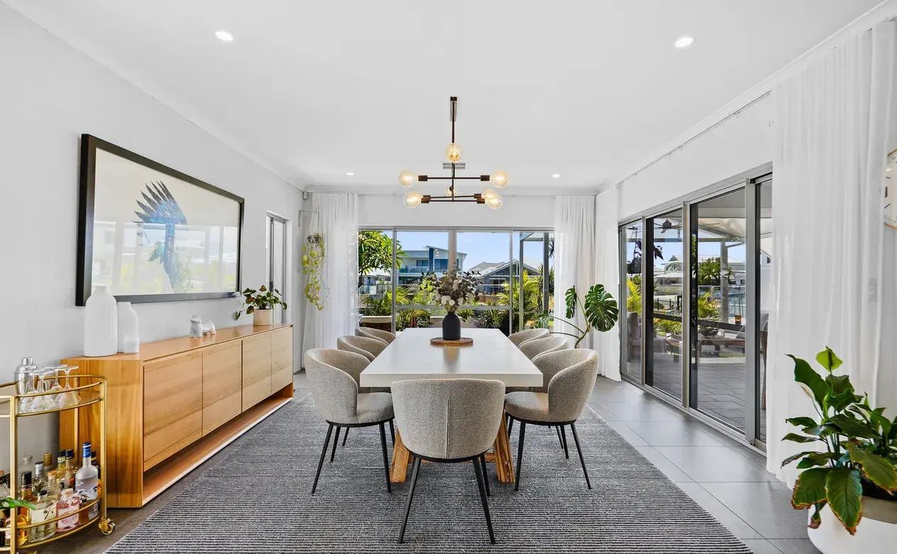 Light-filled dining room with a timber sideboard and glass doors opening to a waterfront alfresco area