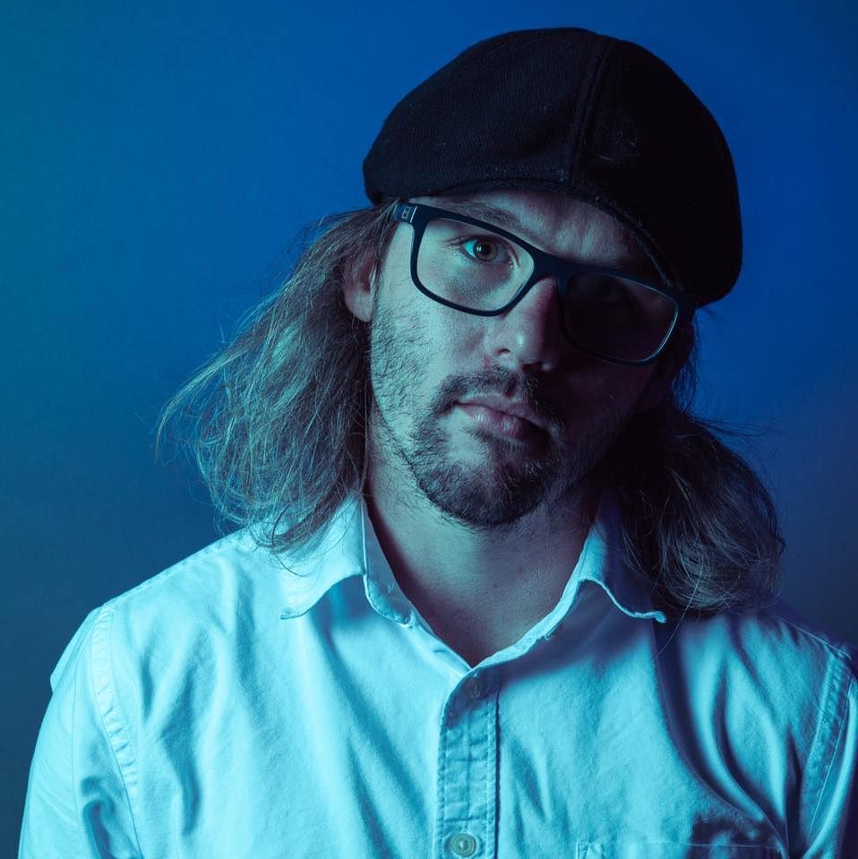a man with long hair wearing glasses and a hat