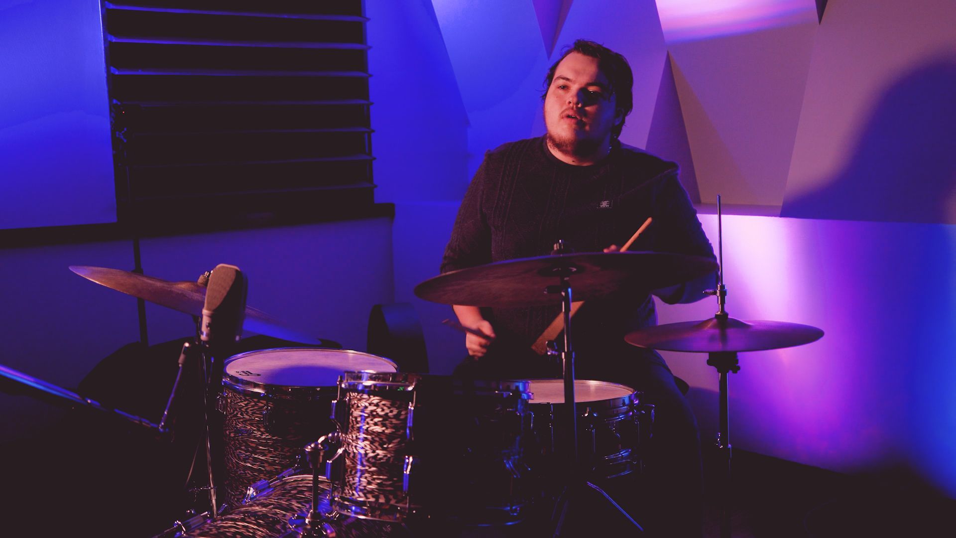 A man is playing drums in a dark room.