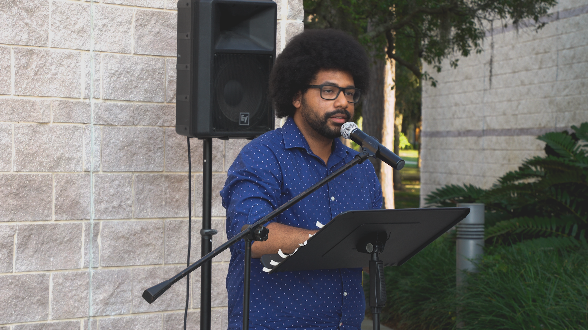 A man in a blue shirt is standing in front of a microphone.
