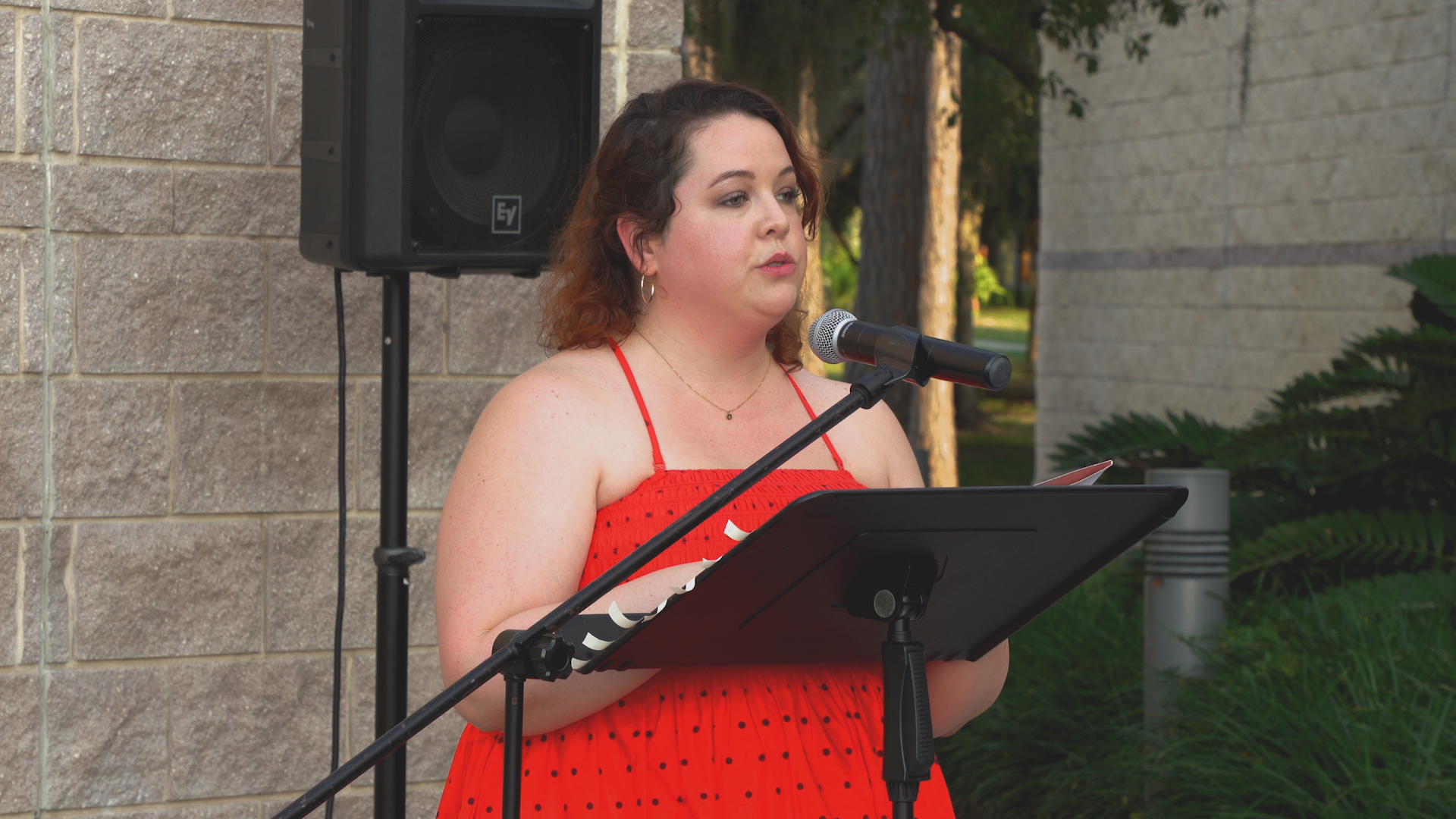 A woman in a red dress is standing at a podium speaking into a microphone.