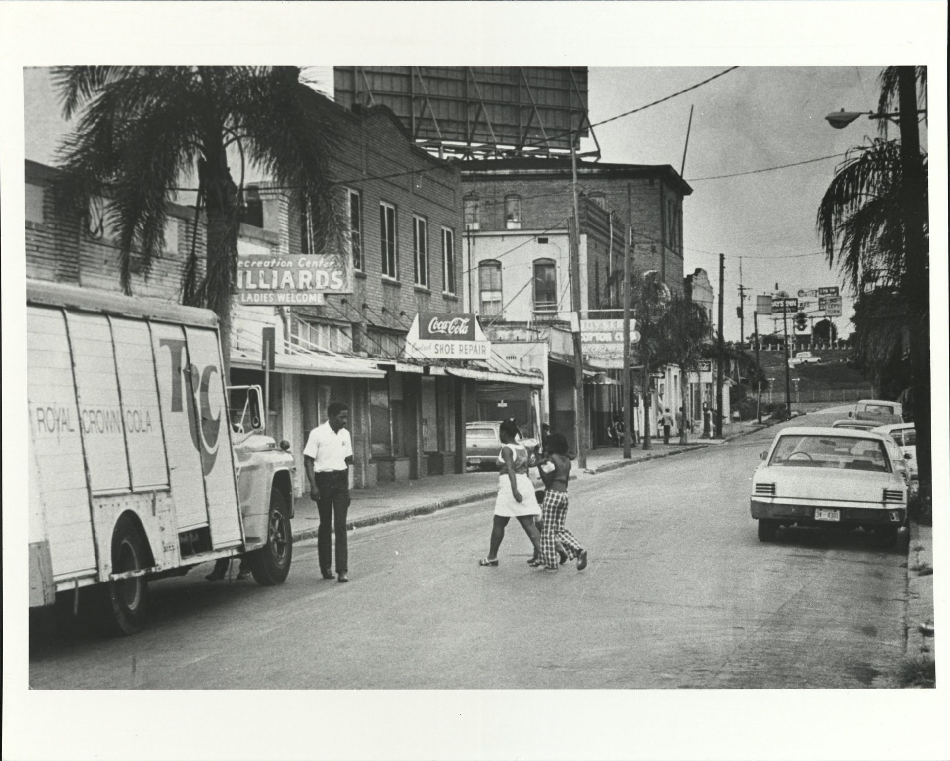 A black and white photo of people crossing a street in front of a building that says illiapoa