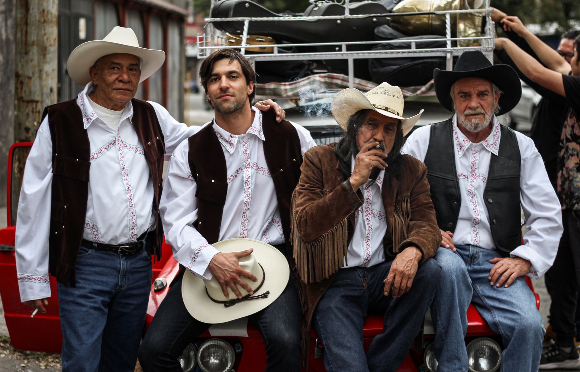 four men in cowboy hats are sitting on a red car