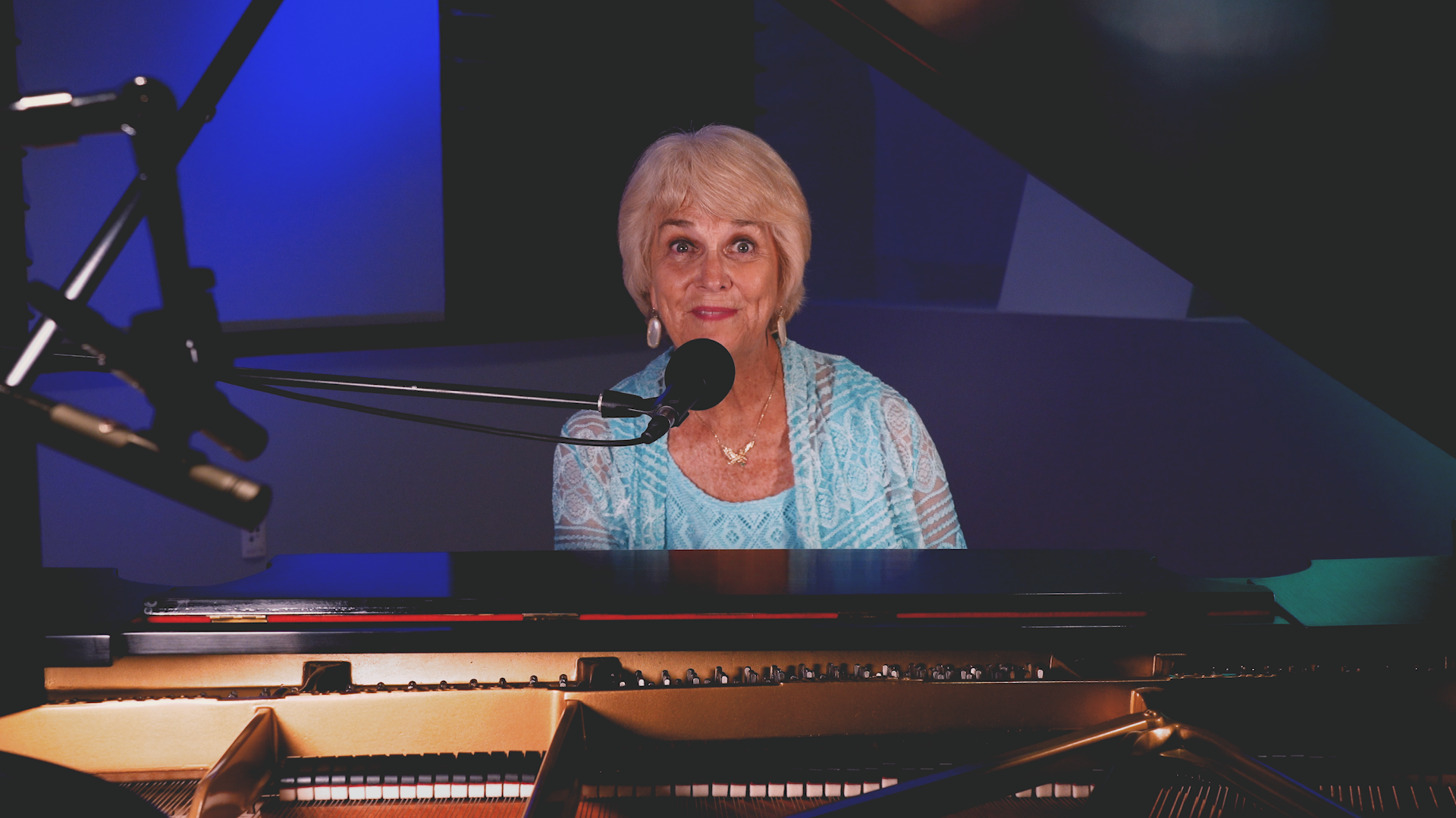 A woman is singing into a microphone while sitting at a piano.