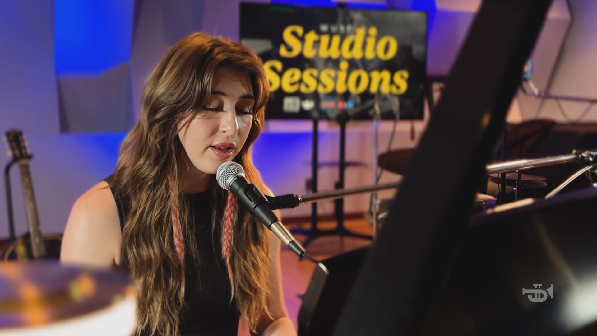 A person singing into a microphone while playing a piano in a music studio, with a