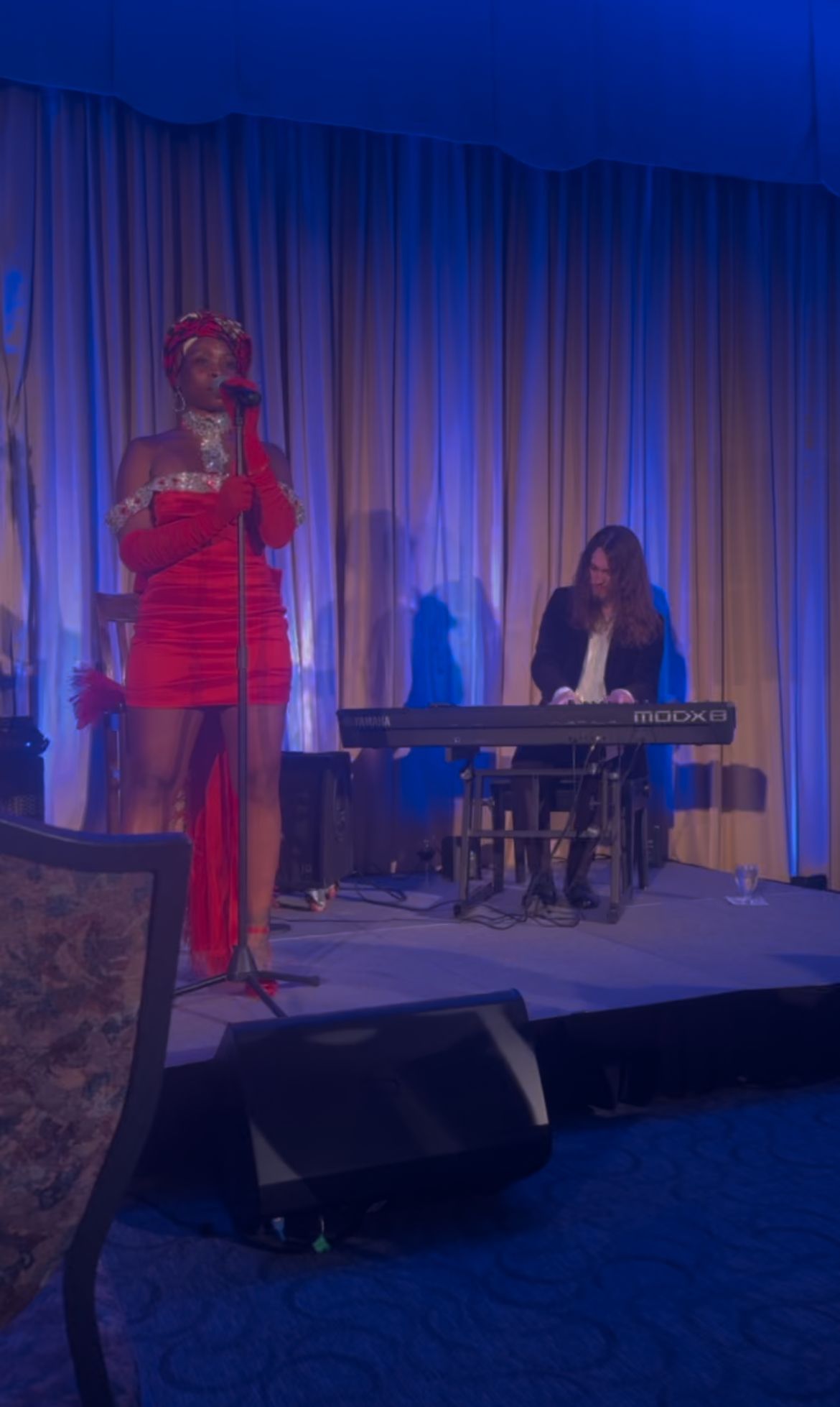 A woman in a red dress is singing into a microphone on a stage.