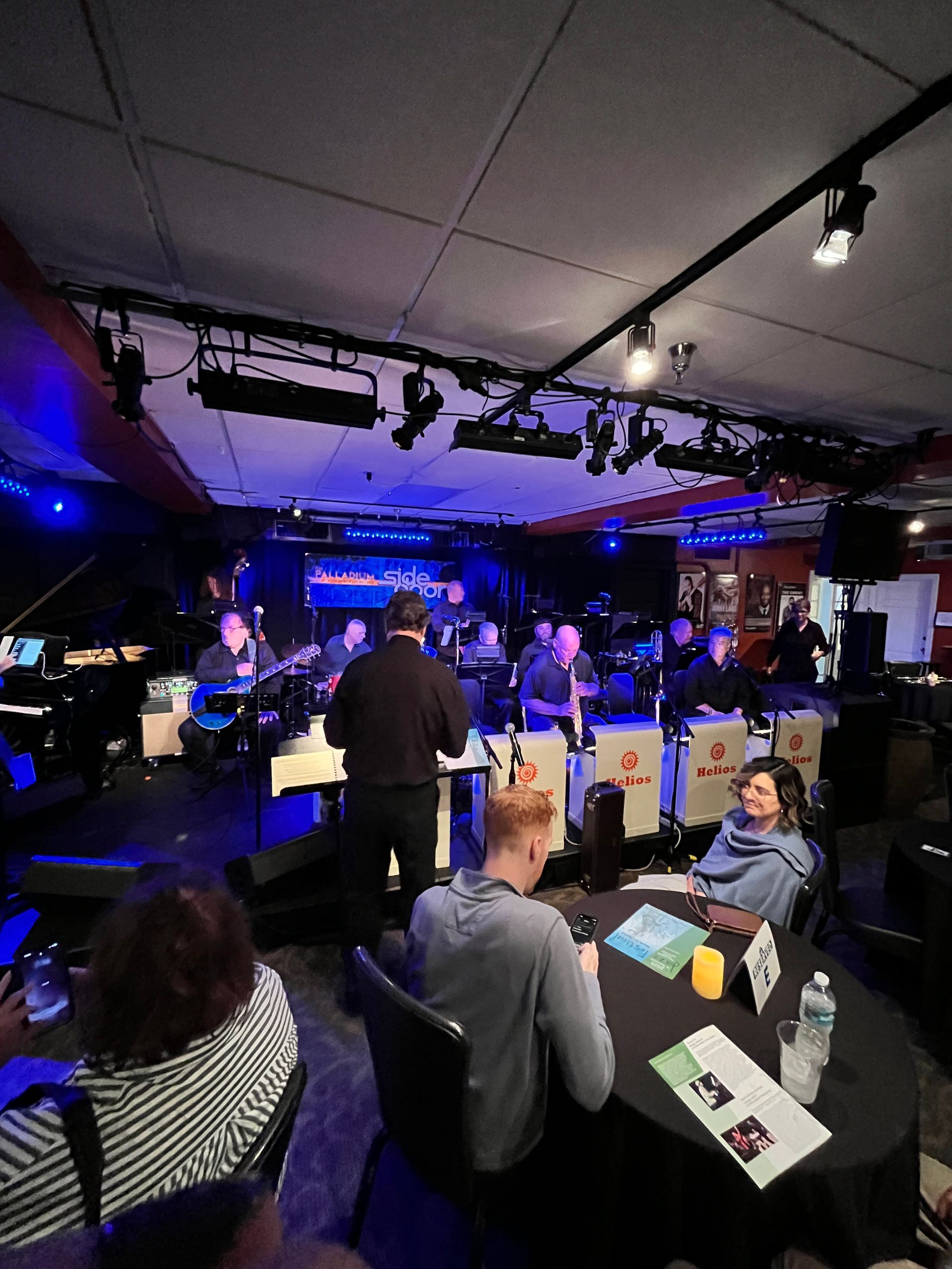 A group of people are sitting at tables in a room with a band on stage.