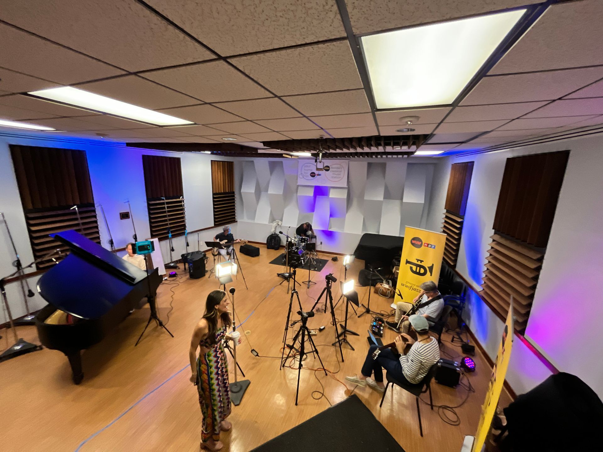 A group of people are standing in a large room with a piano.
