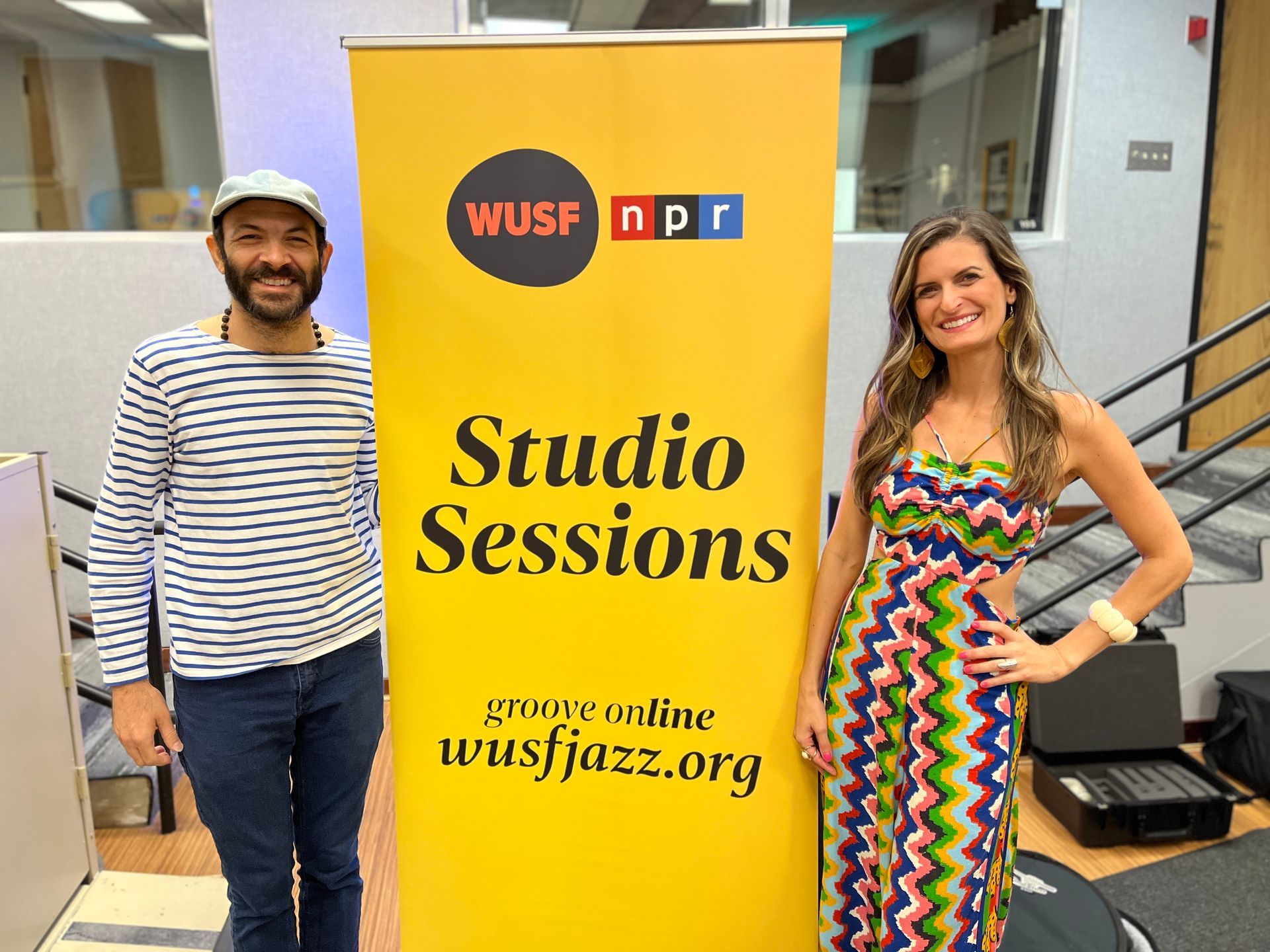 A man and a woman standing next to a yellow sign that says studio sessions