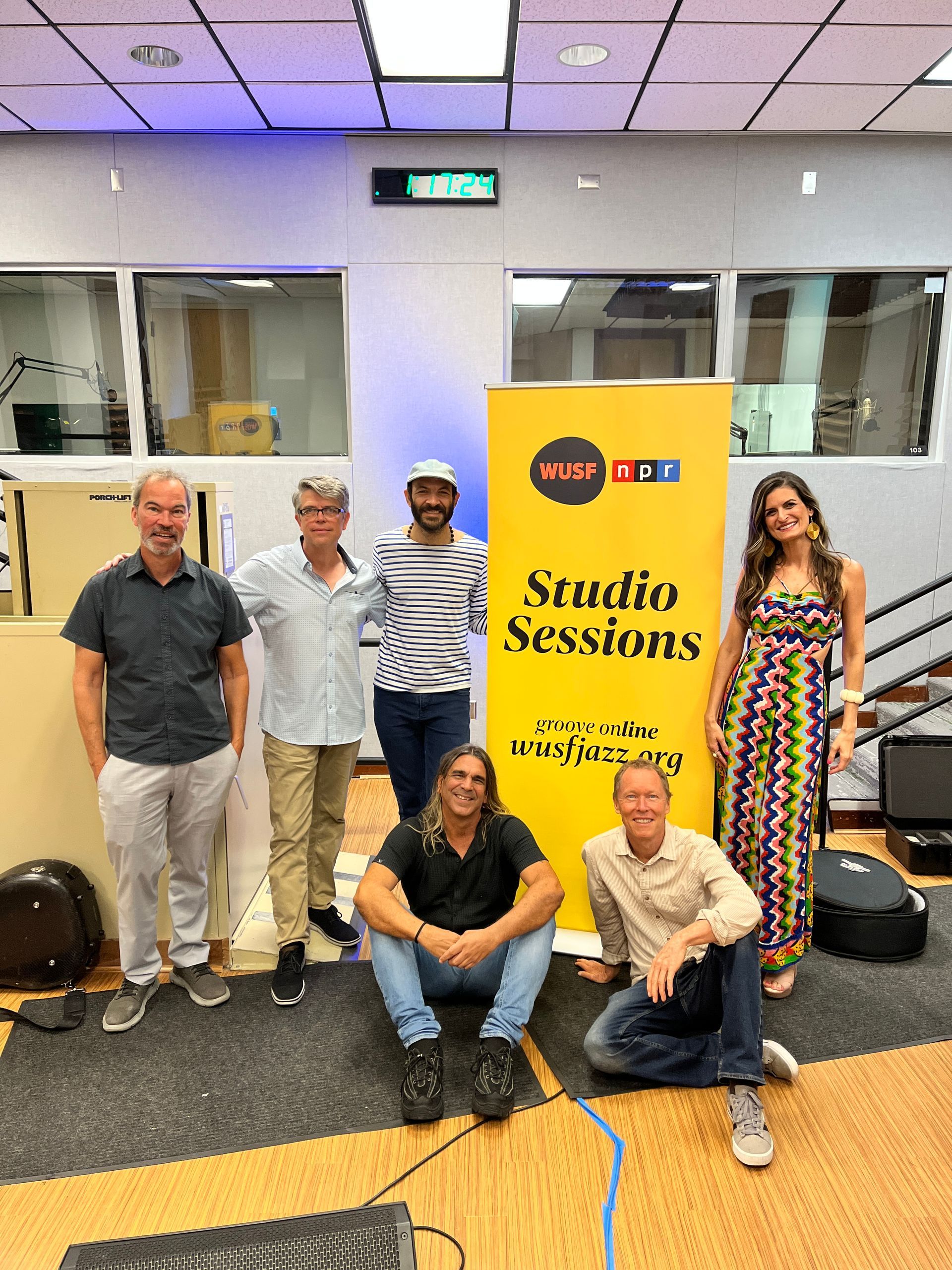 A group of people are posing for a picture in front of a yellow sign that says studio sessions.