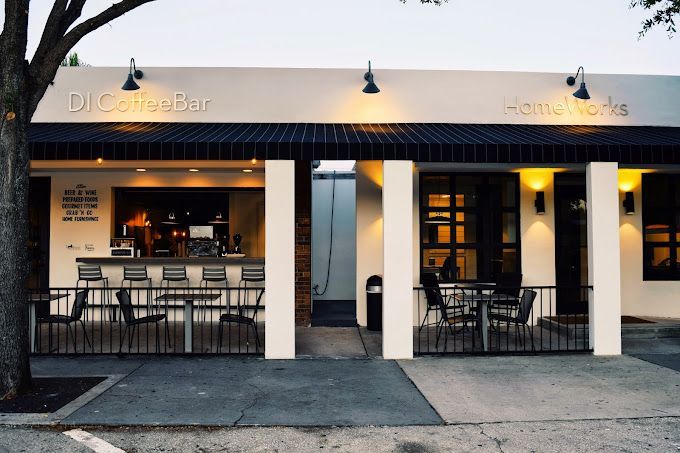 A white building with a black awning and tables and chairs outside