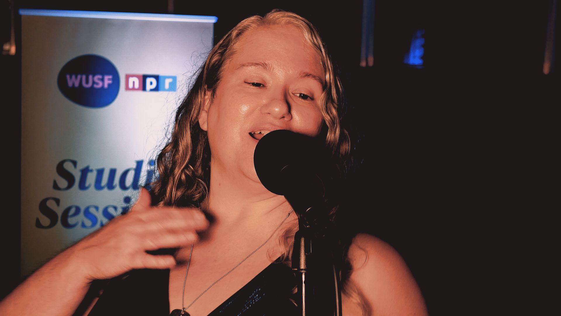 A woman singing into a microphone in front of a sign that says studio session