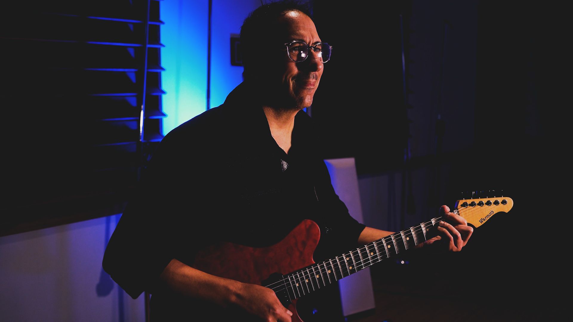 A man is playing an electric guitar in a dark room.
