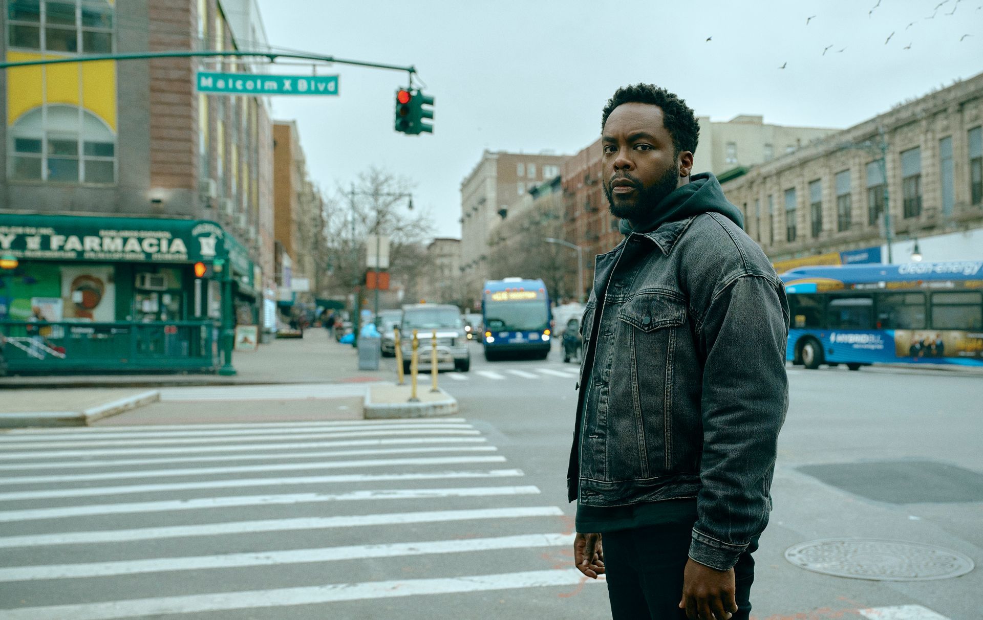 a man is standing on the corner of a city street named Malcolm X Blvd.