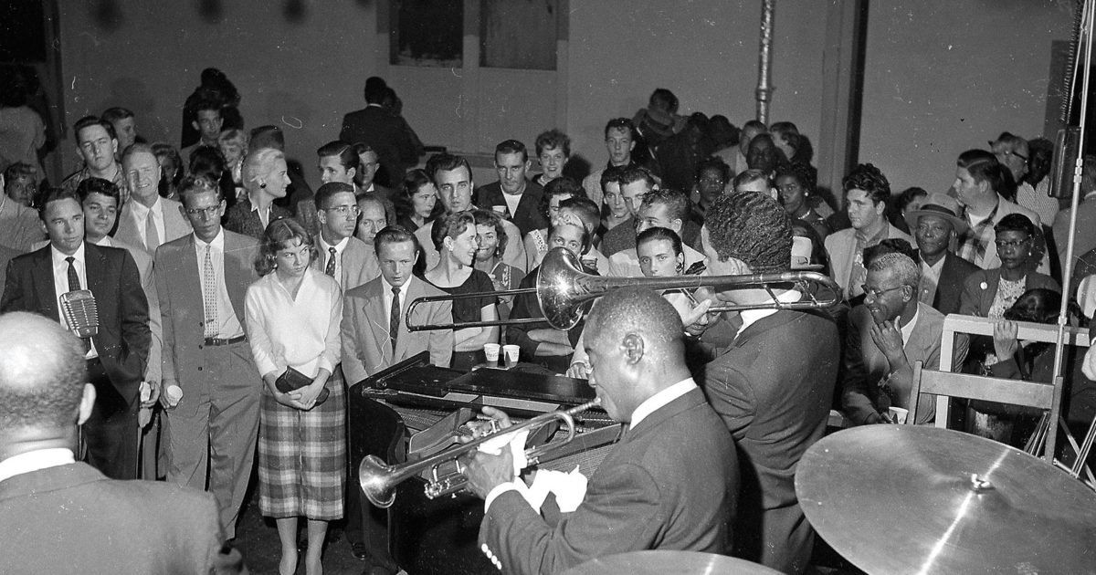 A man is playing a trumpet in front of a crowd of people.