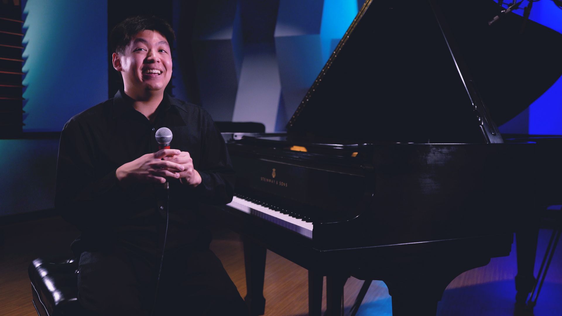 A man is sitting in front of a piano holding a microphone.