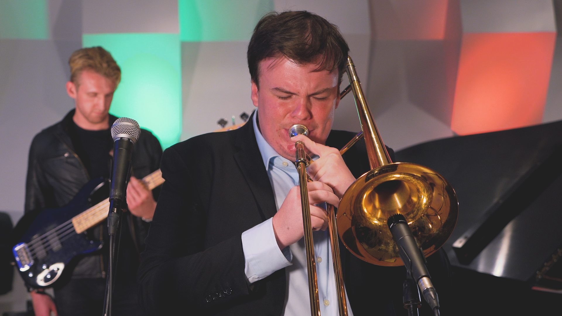 A man in a suit is playing a trombone in front of a microphone.