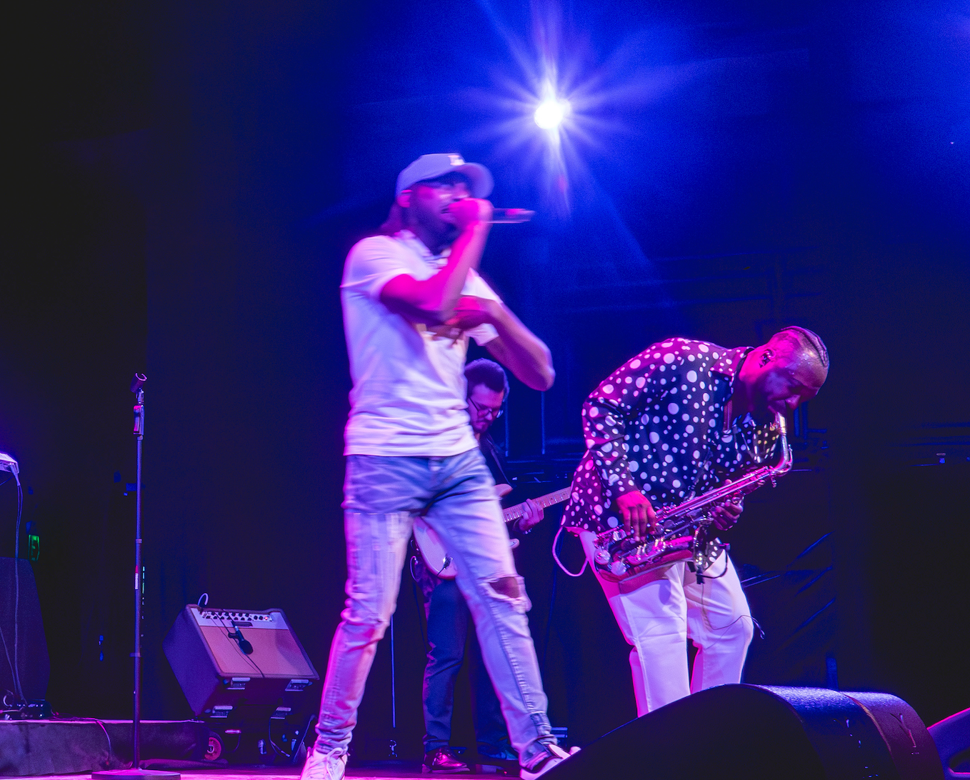 A man is singing into a microphone on a stage while another man plays a saxophone.
