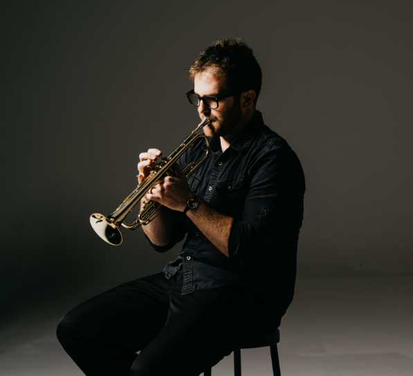 A man is sitting on a stool playing a trumpet