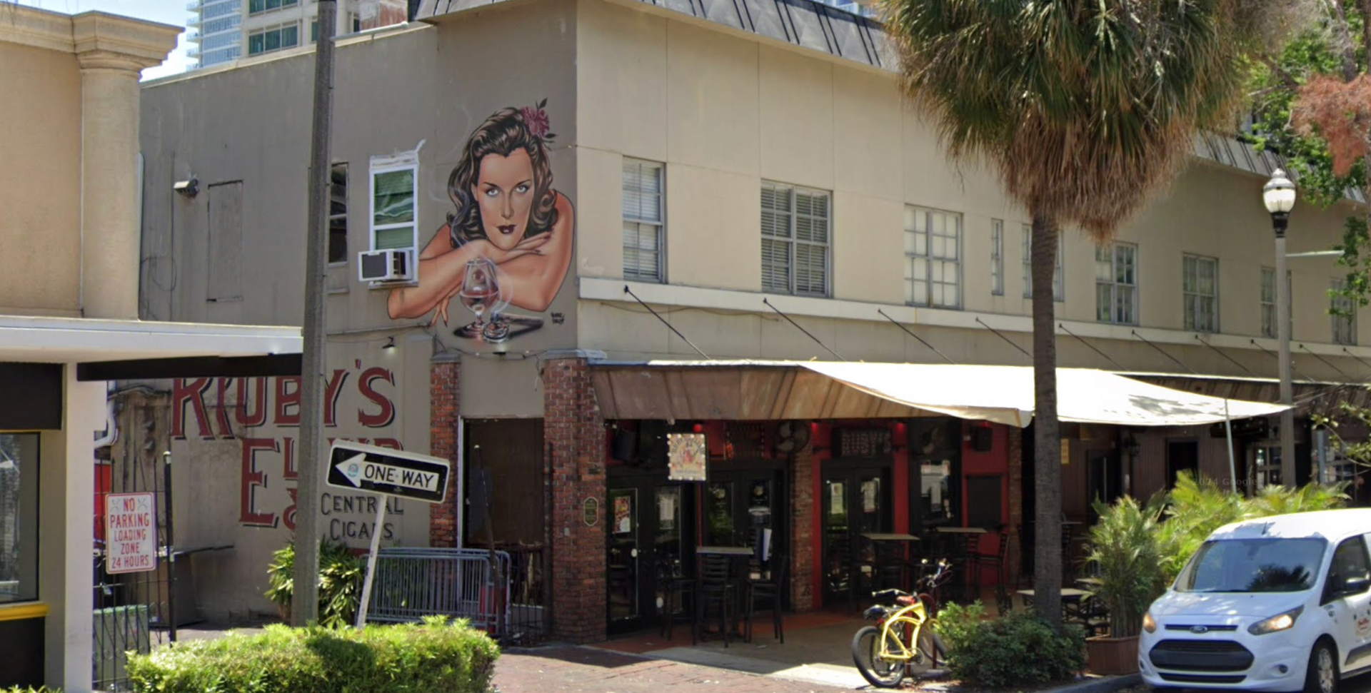 A white van is parked in front of a building with a mural of a woman on the side.