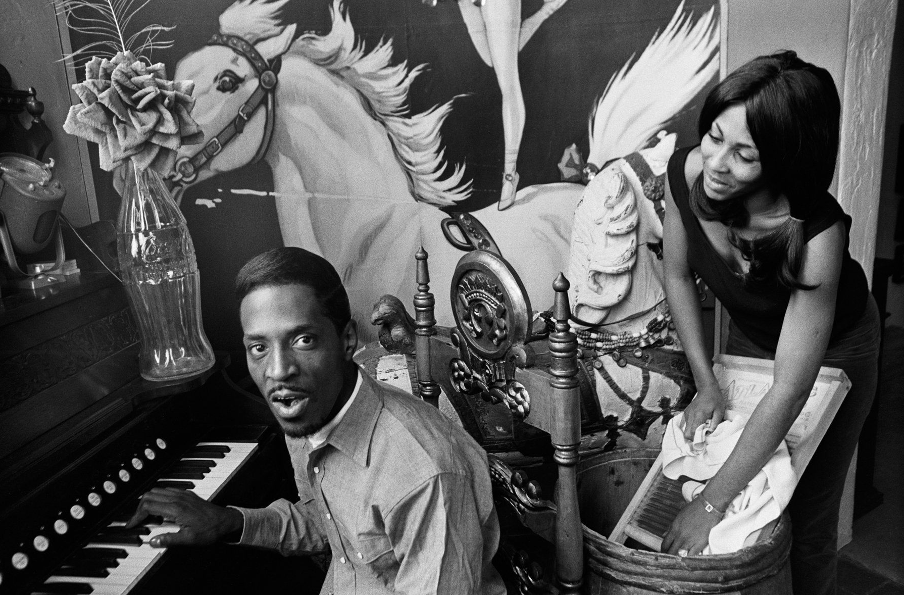 A man is playing a piano and a woman is standing next to him.