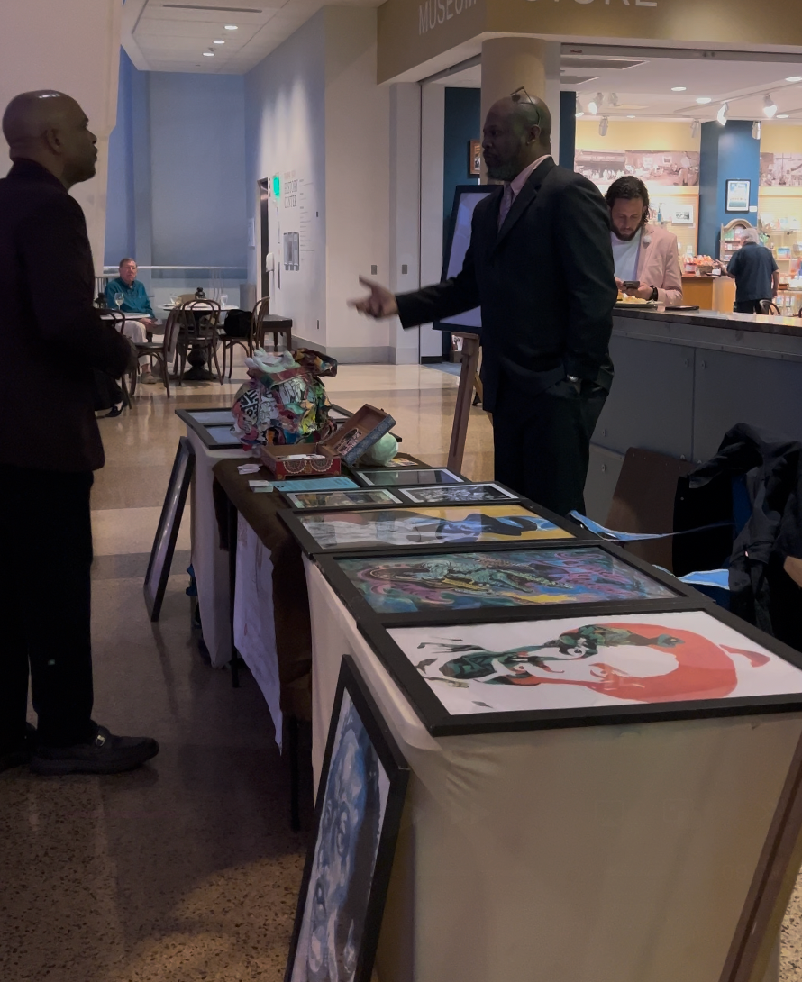 A man in a suit stands in front of a table with paintings on it