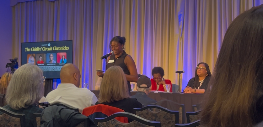 A woman is giving a presentation to a group of people sitting at a table.