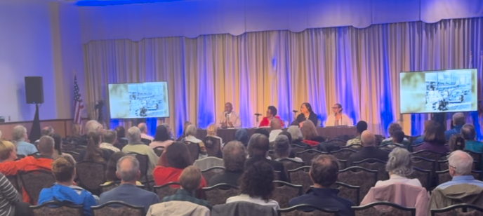 A large group of people are sitting in a conference room watching a presentation.