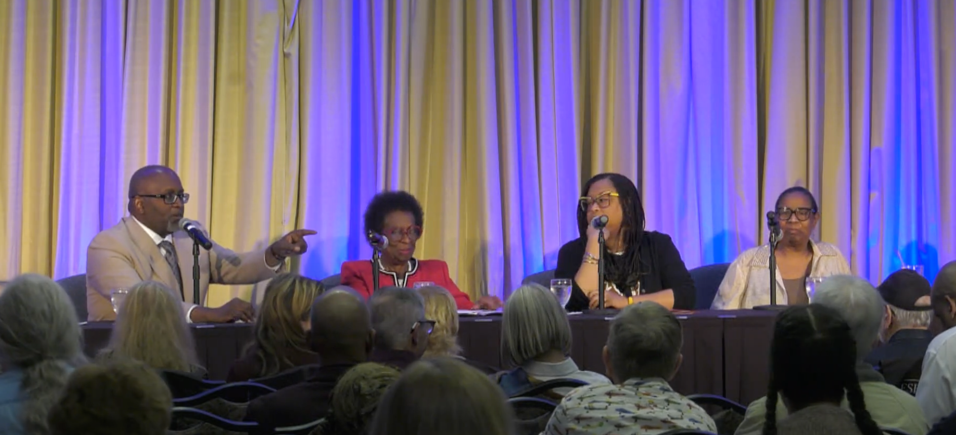 A group of people are sitting at a table in front of a microphone.